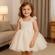 Babelio toddler girl in white princess summer dress with bows, smiling in living room