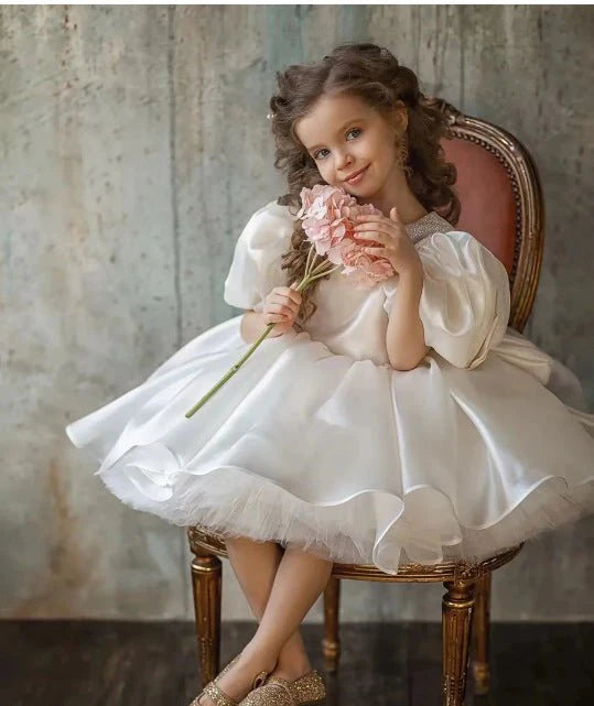 Babelio girl in a white puffy flower dress on chair, holding pink flowers in a vintage room