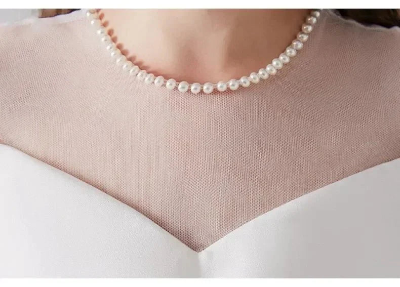 Babelio close-up of white dress with sheer neckline and pearl necklace, formal occasion wear